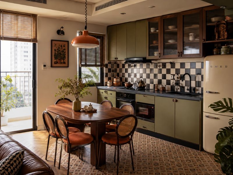 Khu bếp và bàn ăn phong cách thiết kế nội thất chung cư Retro với tủ bếp xanh olive, gạch ốp caro, bàn ăn gỗ tròn và tủ lạnh kiểu cổ điển