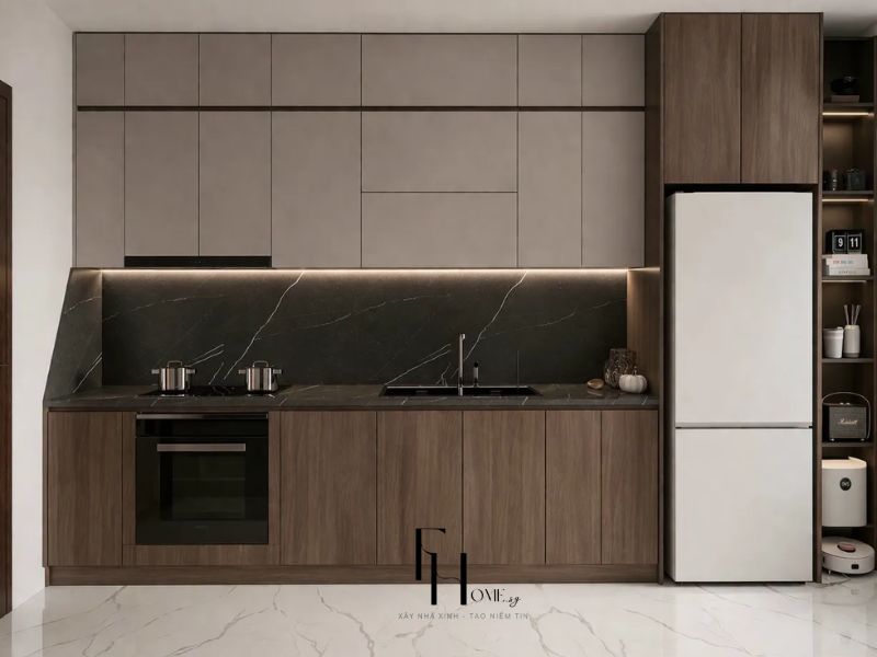 Phòng bếp chung cư 55m2 với 2 phòng ngủ, tủ trên xám taupe kết hợp tủ dưới gỗ walnut, ốp tường đá marble đen vân trắng và tủ lạnh trắng tích hợp