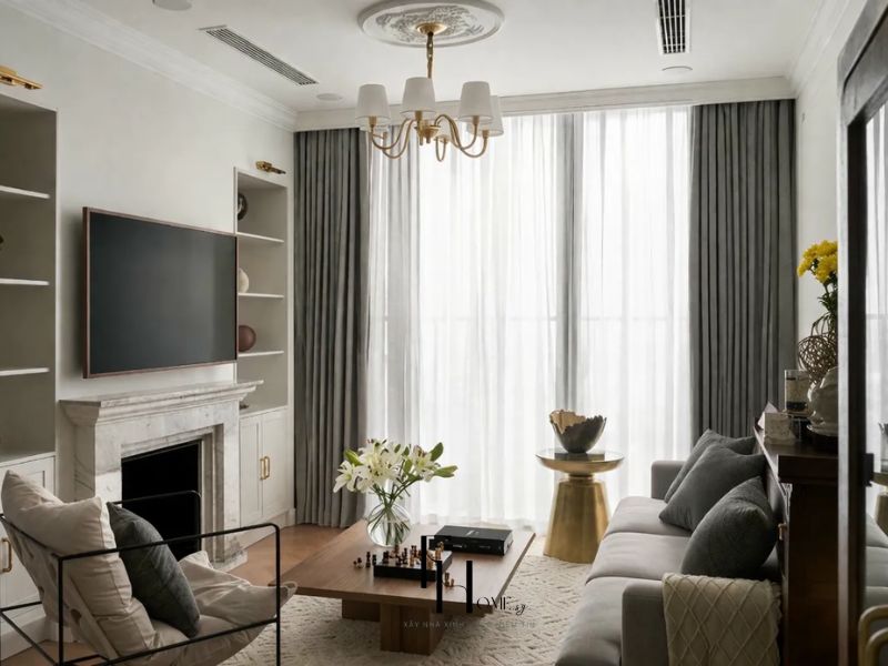 Phòng khách chung cư 55m2 phong cách Scandinavian với hệ kệ tivi trắng đối xứng, lò sưởi ốp đá marble và đèn chùm vàng gold