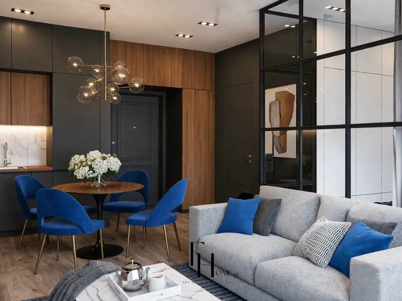 Phòng khách liên thông bếp chung cư 100m2 vách kính khung thép đen phân tách không gian sofa xám gối xanh cobalt bàn ăn tròn gỗ 4 ghế nhung xanh và đèn thả quả cầu kính chân đồng