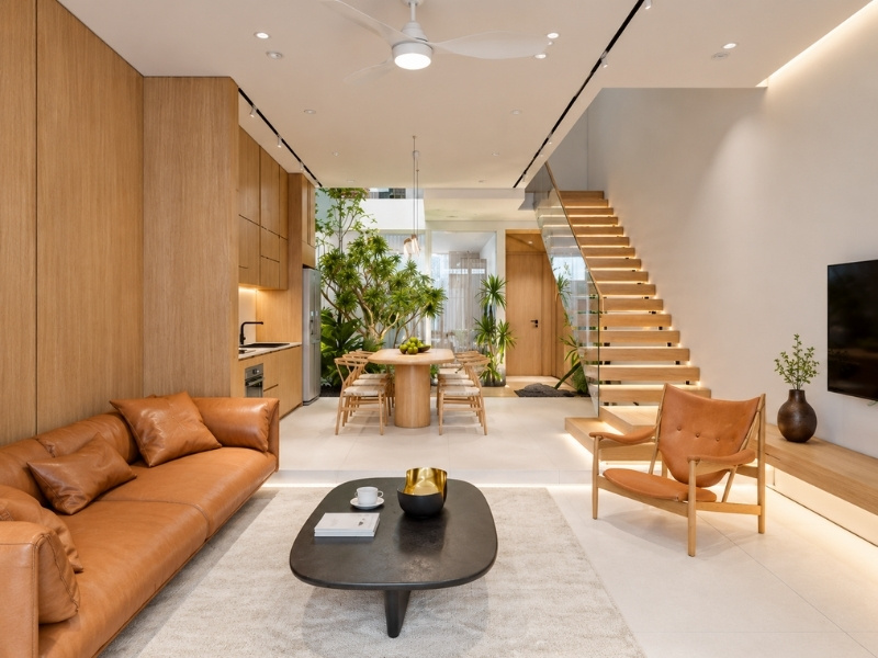 Phòng khách nhà phố phong cách Bắc Âu với sofa da nâu bò và cầu thang lan can kính