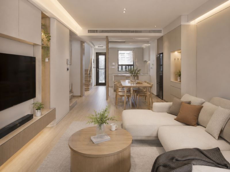 Phòng khách nhà phố phong cách Đài Loan với sofa chữ L màu kem, bàn trà tròn, bàn ăn gỗ sáng và không gian liên thông gọn gàng