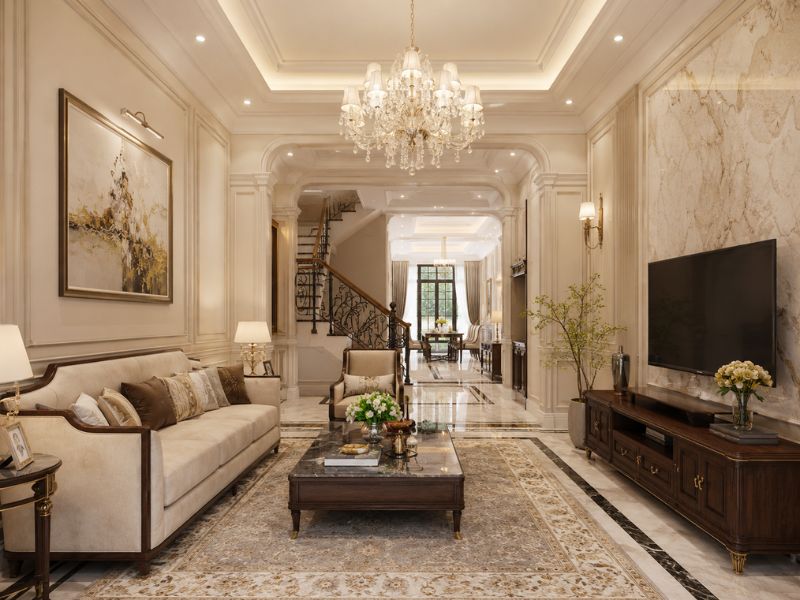 Phòng khách nhà phố phong cách Tân Cổ Điển với đèn chùm pha lê, sofa lớn, bàn trà mặt đá và mảng tường trang trí đối xứng
