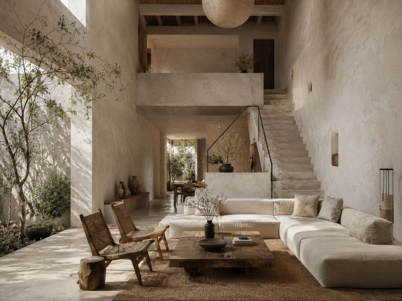 Phòng khách nhà phố phong cách Wabi Sabi với trần cao, cầu thang bê tông, sofa thấp và sân vườn trong nhà
