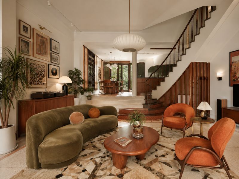 Phòng khách nhà phố phong cách thiết kế nội thất Retro với sofa cong màu xanh rêu, ghế bành cam đất, bàn trà gỗ và mảng tranh treo tường cá tính