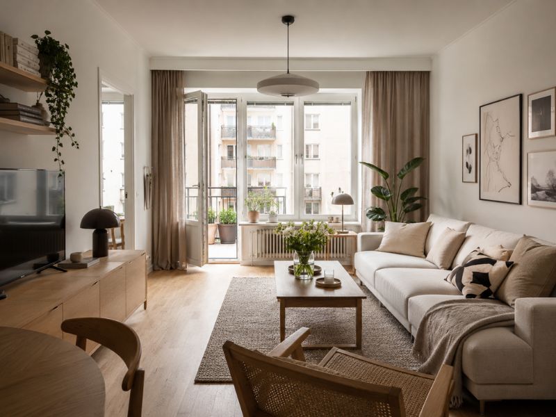 Phòng khách phong cách thiết kế nội thất chung cư Bắc Âu với sofa sáng màu, bàn trà gỗ, thảm dệt và cửa kính đón ánh sáng tự nhiên
