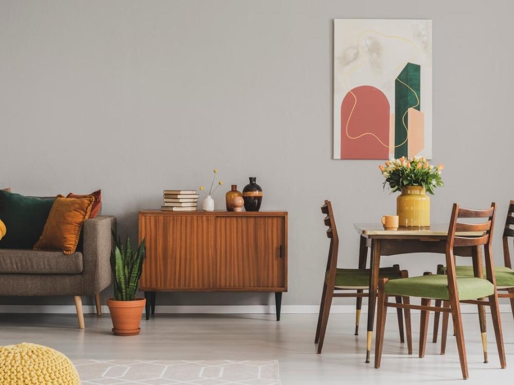 Phòng khách với ghế sofa màu xám có đường nét cong, bàn cà phê chân kim loại mảnh mai, thảm họa tiết hình học và đèn lava đặc trưng