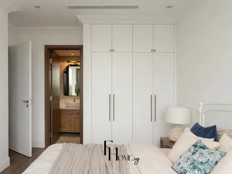 Phòng ngủ chung cư 50m2 phong cách Địa Trung Hải với tường trắng ngà phào chỉ viền trần, giường gỗ trắng nan dọc, gối xanh coban và tủ áo âm tường 6 cánh trắng tay nắm mạ đồng