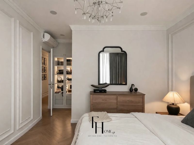 Phòng ngủ chung cư 55m2 phong cách Scandinavian với tường ốp phào trắng, tủ gỗ walnut ngăn kéo và phòng thay đồ kính đèn hắt