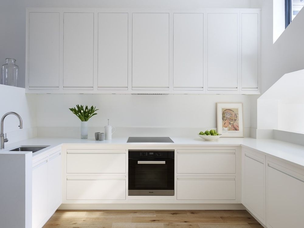 Bếp tối giản trắng toàn bộ, hệ tủ phẳng đồng bộ và bề mặt bếp sạch gọn gàng