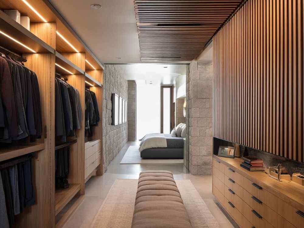Không gian phòng ngủ nối liền phòng thay đồ gỗ sáng, trần ốp lam và tường đá thô mộc