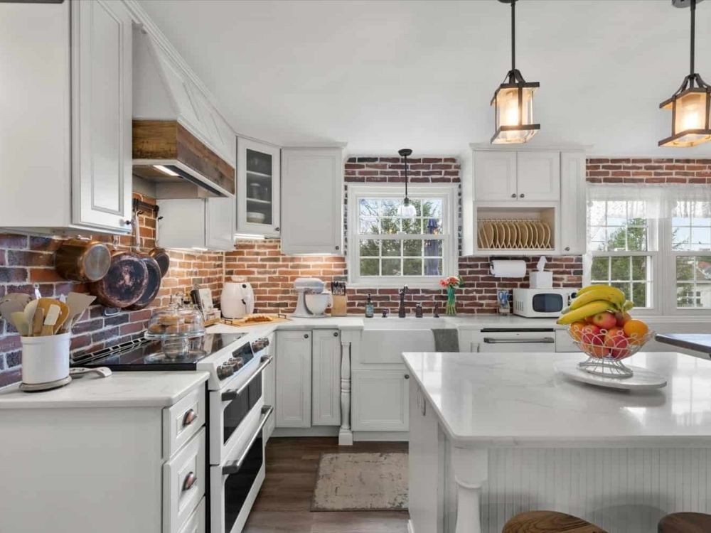 Khu vực nấu với tường gạch lộ, tủ trắng, đảo bếp lớn