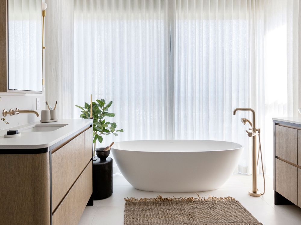 Nhà vệ sinh chung cư với bồn tắm, rèm cửa mỏng đủ để ánh sáng chiếu vào