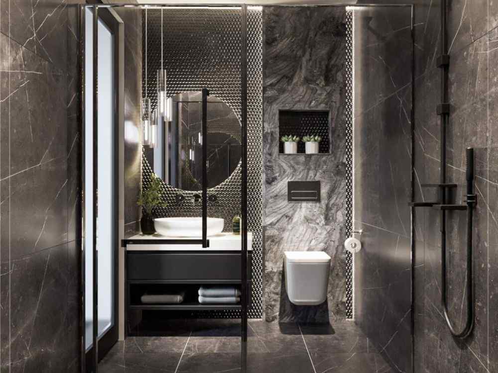 Nhà vệ sinh tông đen hiện đại với tường ốp đá và gạch mosaic ánh kim, gương tròn lớn tạo điểm nhấn