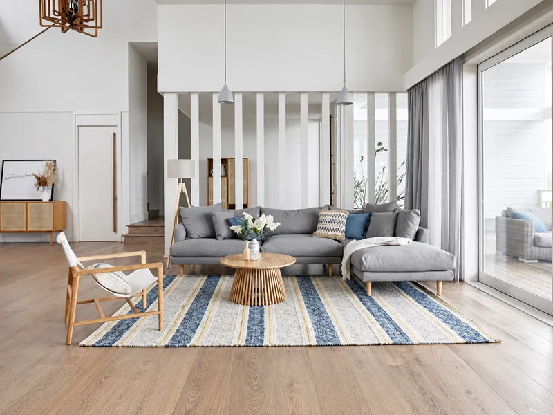 Nội thất phòng khách phong cách Coastal phối sofa xám với thảm sọc xanh trắng gần cửa kính rộng.