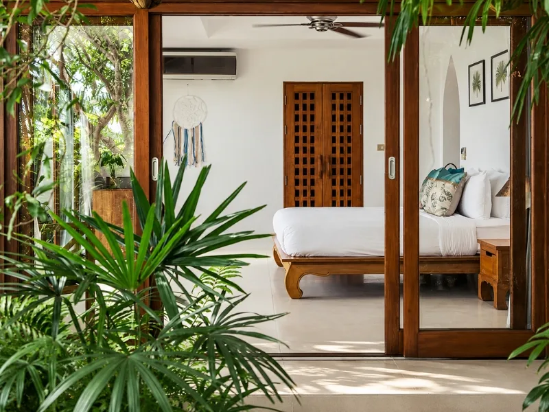 Nội thất phòng ngủ phong cách Tropical sử dụng đồ gỗ cạnh cửa mở ra vườn cây nhiệt đới.