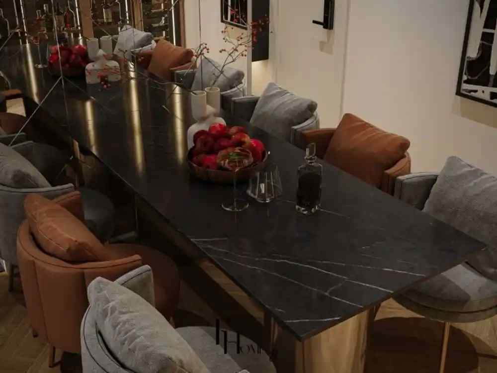 Phòng ăn hiện đại với bàn dài mặt đá đen, ghế bọc nệm màu ghi và nâu, bình hoa và trái cây trang trí