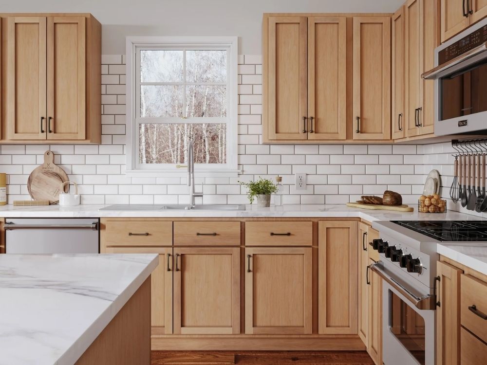 Phòng bếp chữ L với tủ gỗ sáng màu, mặt bàn đá trắng, backsplash ốp gạch thẻ