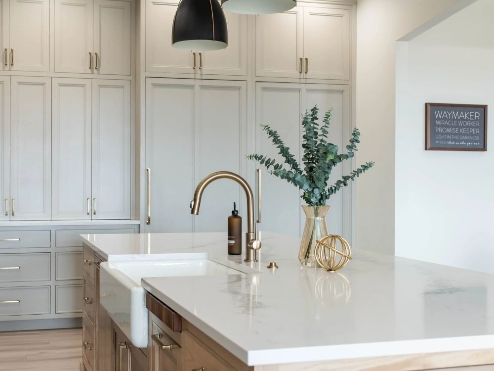 Phòng bếp hiện đại ánh sáng tự nhiên với mặt đá trắng, vòi vàng đồng