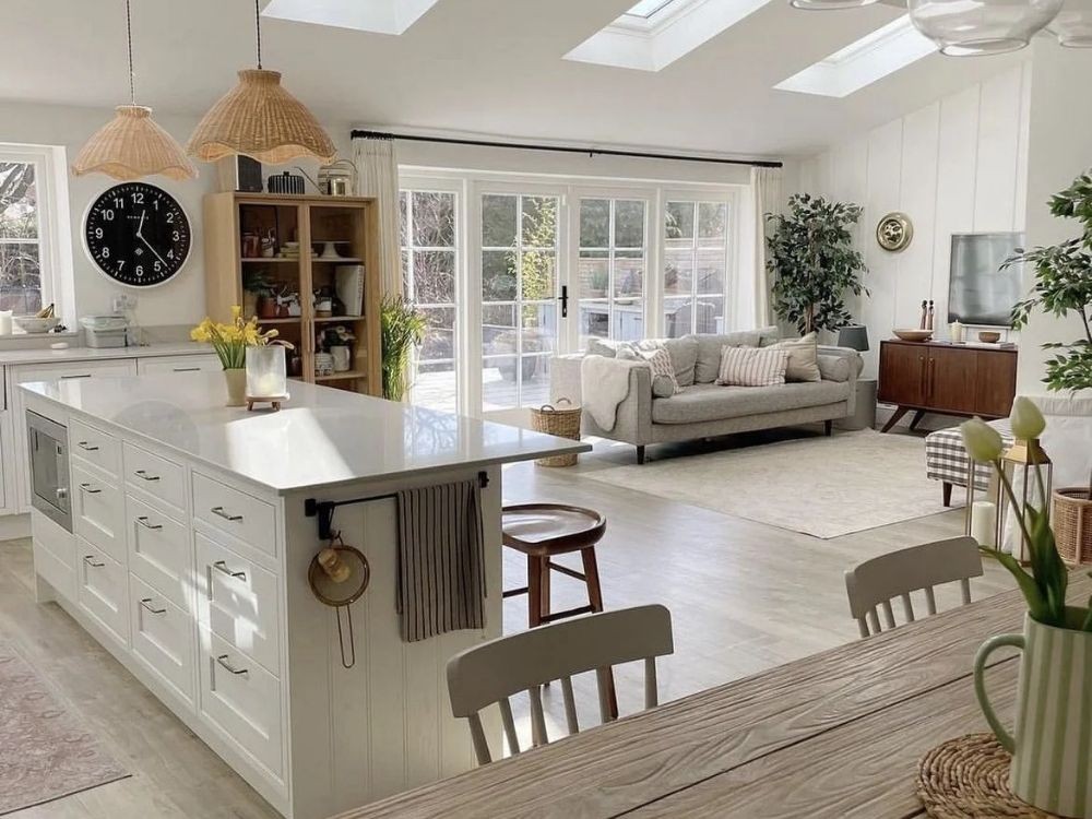 Phòng bếp liền phòng khách với đảo bếp trắng, ghế gỗ sáng, đèn mây tre