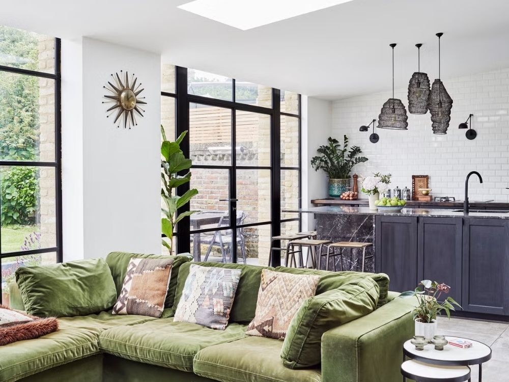 Phòng bếp liên thông phòng khách với sofa nhung xanh, quầy bếp ốp đá đen