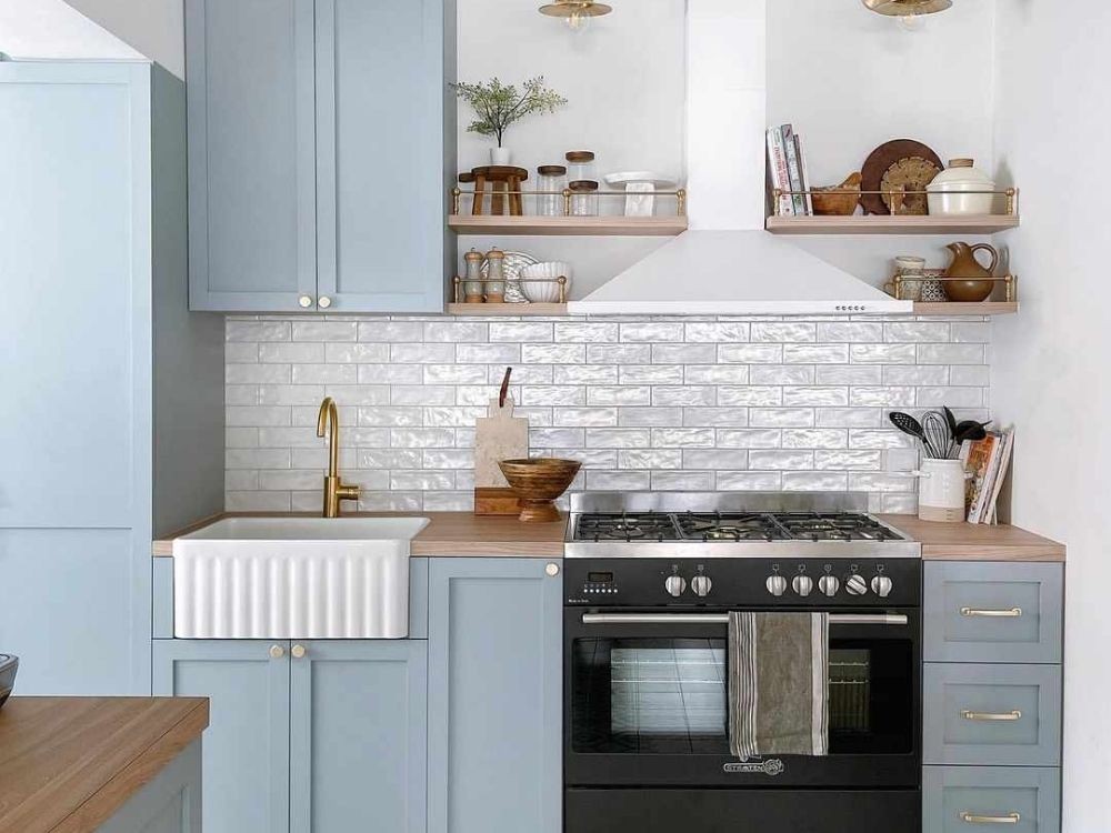 Phòng bếp màu xanh pastel, gạch ốp trắng bóng, kệ gỗ mở và vòi nước mạ vàng