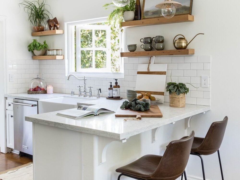 Phòng bếp sáng với quầy bar mini mặt đá trắng, kệ gỗ treo tường