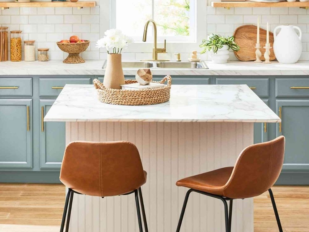 Phòng bếp sáng với quầy bar mini mặt đá vân mây, ghế da nâu, tủ xanh pastel