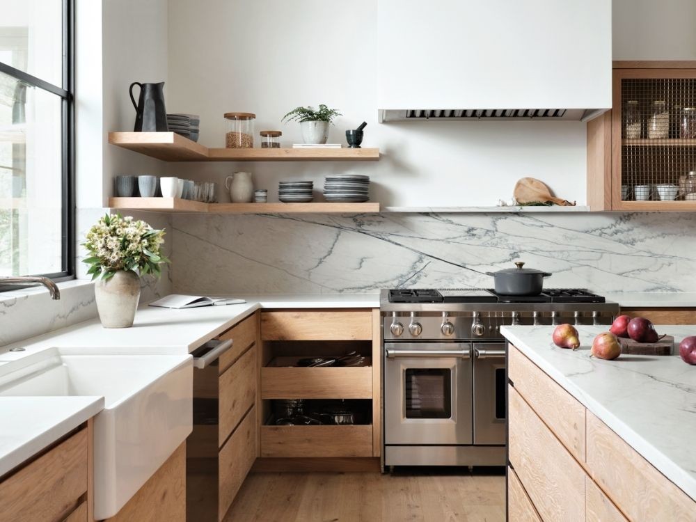 Phòng bếp tối giản với tủ gỗ sáng, bề mặt đá trắng vân nhẹ và kệ mở trang trí nhẹ nhàng