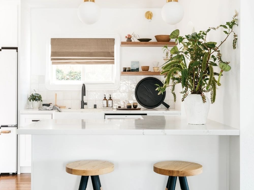 Phòng bếp trắng trang nhã, quầy bar mini rộng rãi, kệ gỗ trưng bày đồ decor