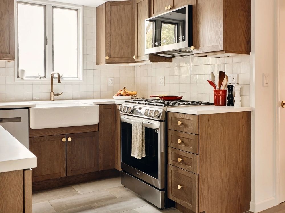 Phòng bếp tủ bếp chữ U gỗ nâu, bồn rửa cạnh cửa sổ, mặt bếp trắng