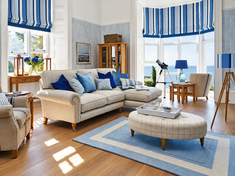 Phòng khách phong cách ven biển có sofa trắng điểm gối xanh trong không gian cửa sổ nhiều nắng.