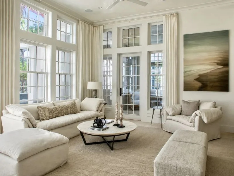 Phòng khách phong cách đương đại bố trí sofa màu kem và bàn trà tròn bên những ô cửa sổ cao.