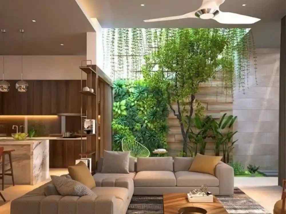 Phòng khách liền bếp có giếng trời xanh mát, tường cây thẳng đứng và sofa nâu nhạt tạo cảm giác thư giãn