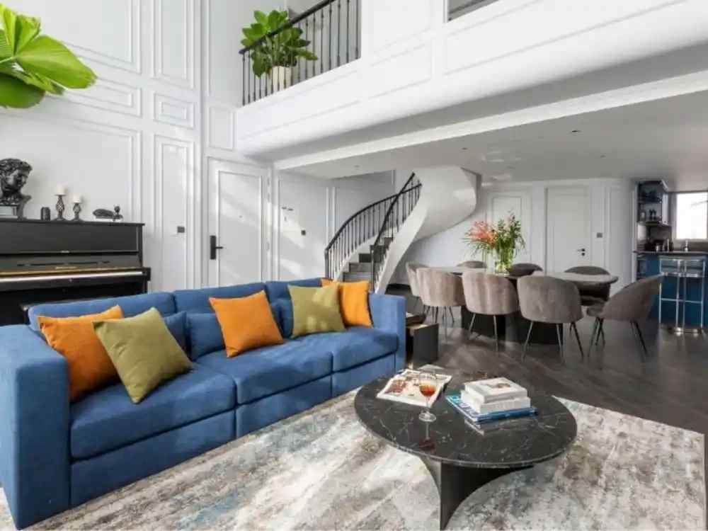 Phòng khách liền bếp hiện đại với sofa xanh nổi bật, bàn đá đen và cầu thang xoắn trắng tinh tế