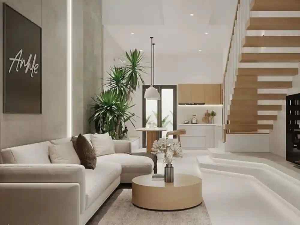 Phòng khách nhà ống tông sáng với sofa kem, cầu thang gỗ treo và bàn tròn gỗ cạnh khu bếp liền kề