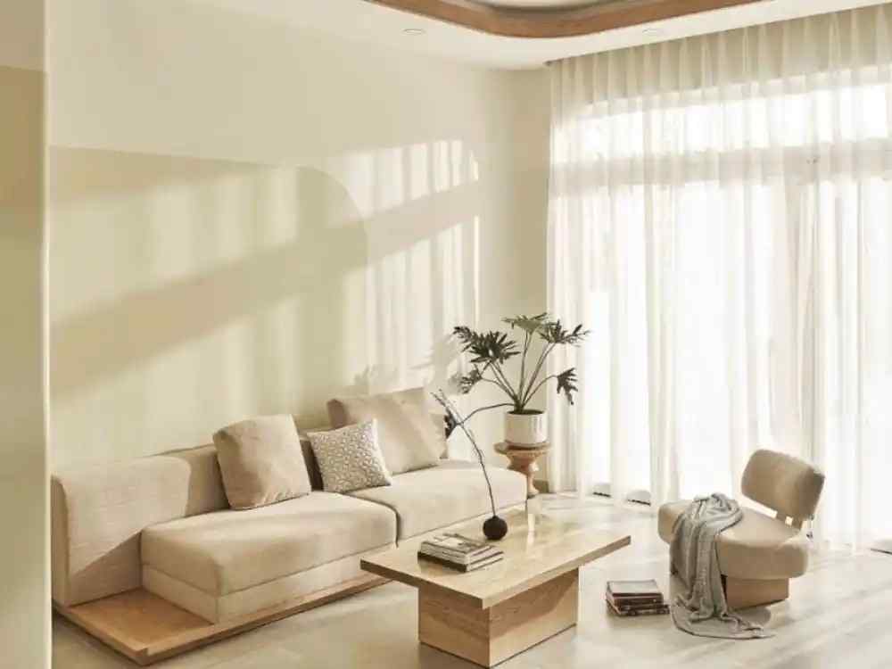 Phòng khách Nhật Bản tối giản, sofa vải be, bàn gỗ thấp vuông, cây xanh cạnh rèm trắng