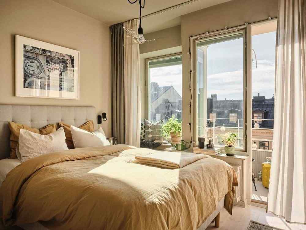 Phòng ngủ ban công phong cách ấm áp, chăn nâu nhạt, cây xanh đặt cạnh