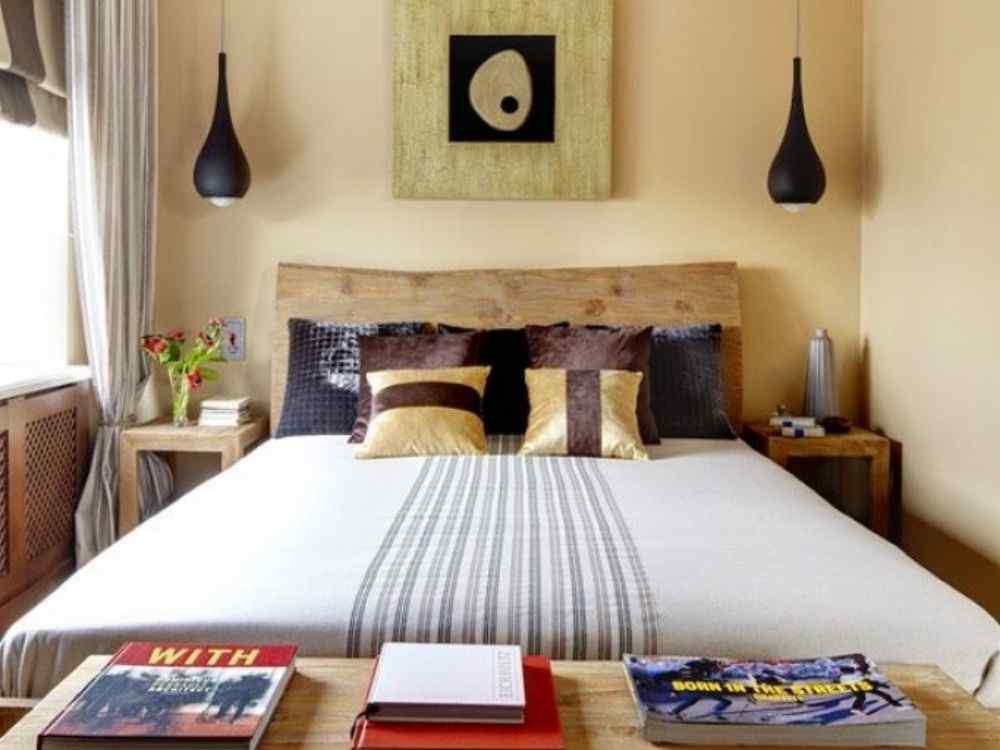 Phòng ngủ giường gỗ đôi, tường vàng ấm, đèn thả đen hai bên, tranh treo và bàn đầu giường có sách