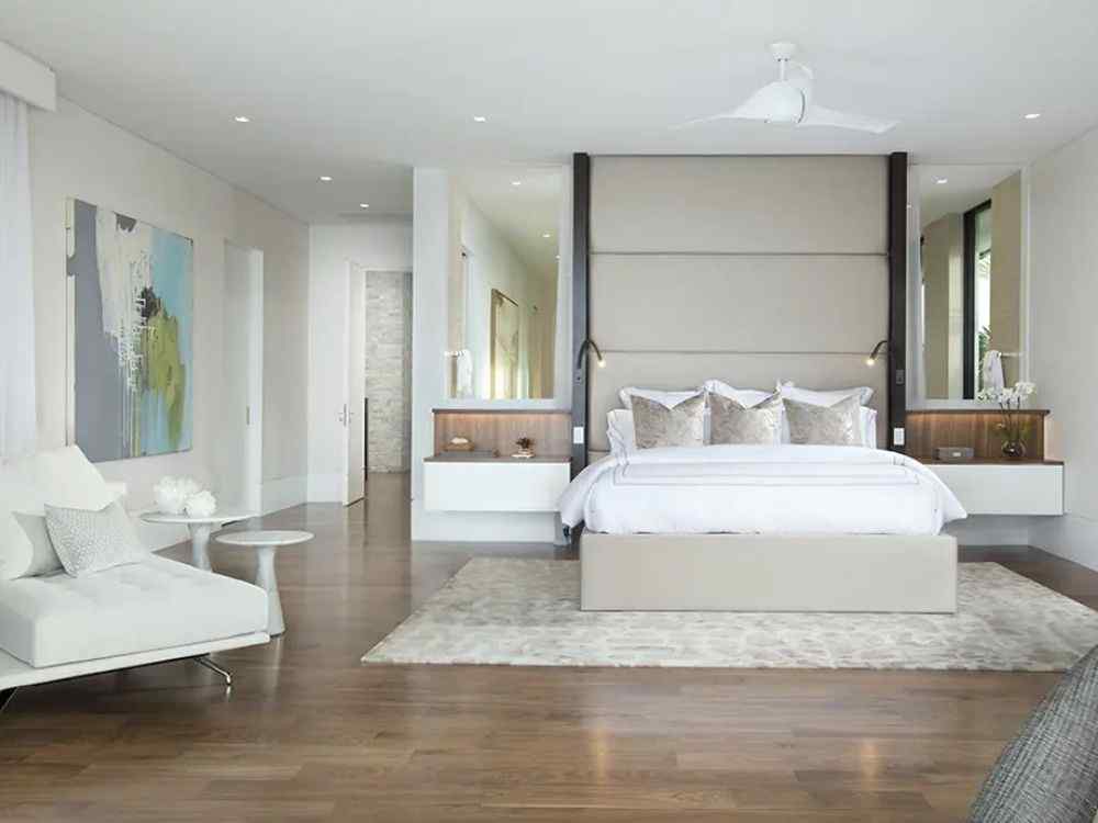 Phòng ngủ master sang trọng với giường bọc nệm màu kem, sàn gỗ nâu, ghế thư giãn