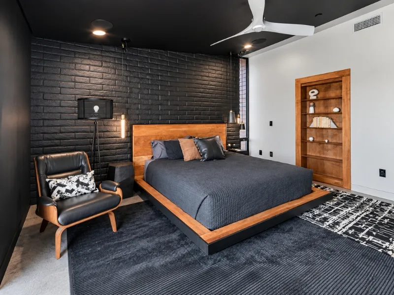Thiết kế phòng ngủ phong cách Mid-Century Modern phối giường gỗ thấp với tường gạch đen và ghế thư giãn.