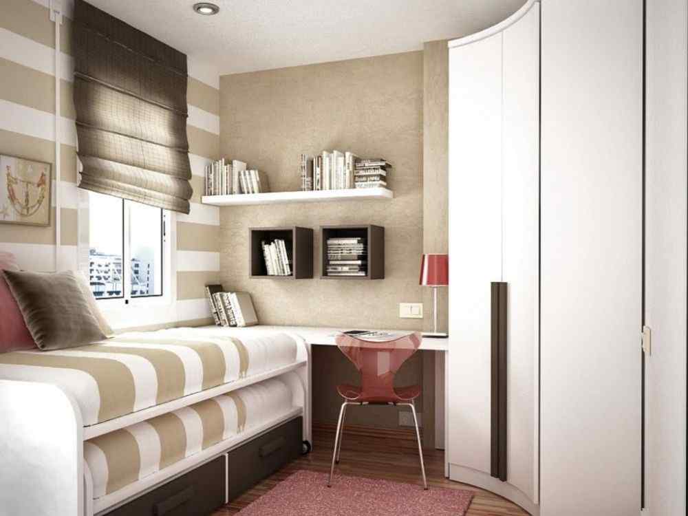 Phòng ngủ nhỏ với giường đơn có hộc kéo, bàn học cạnh tủ cong, kệ sách treo và rèm roman nâu
