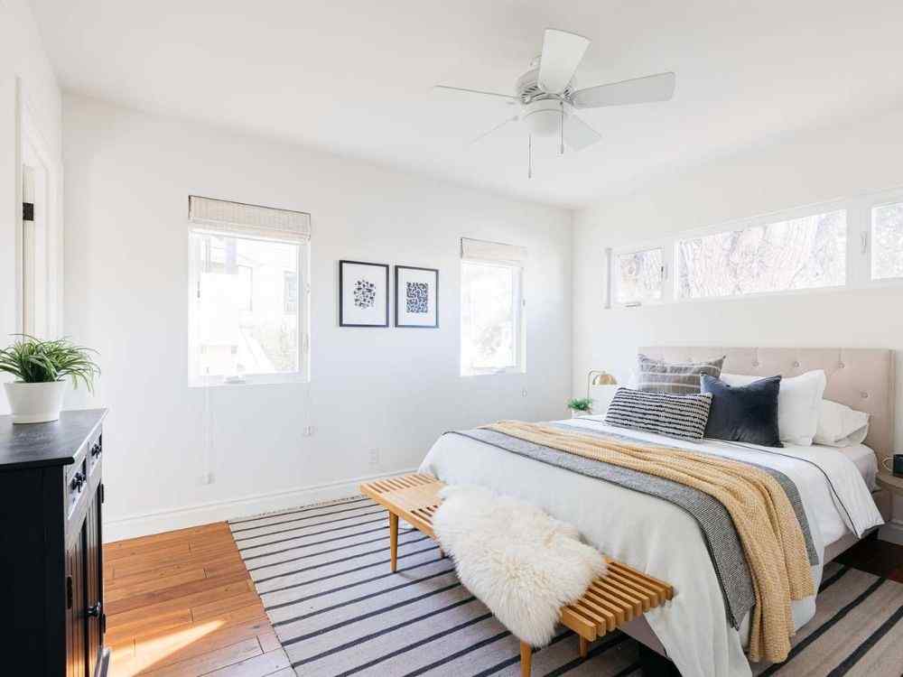 Phòng ngủ thoáng sáng với cửa sổ lớn, giường bọc nệm trung tính và ghế gỗ đầu giường