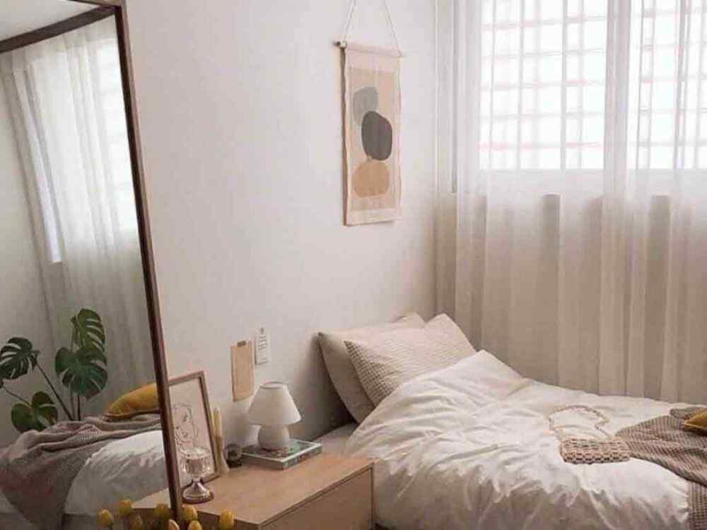 Phòng ngủ tối giản với giường đơn sát tường, ga trắng, rèm voan trắng, gương dựa tường và cây xanh