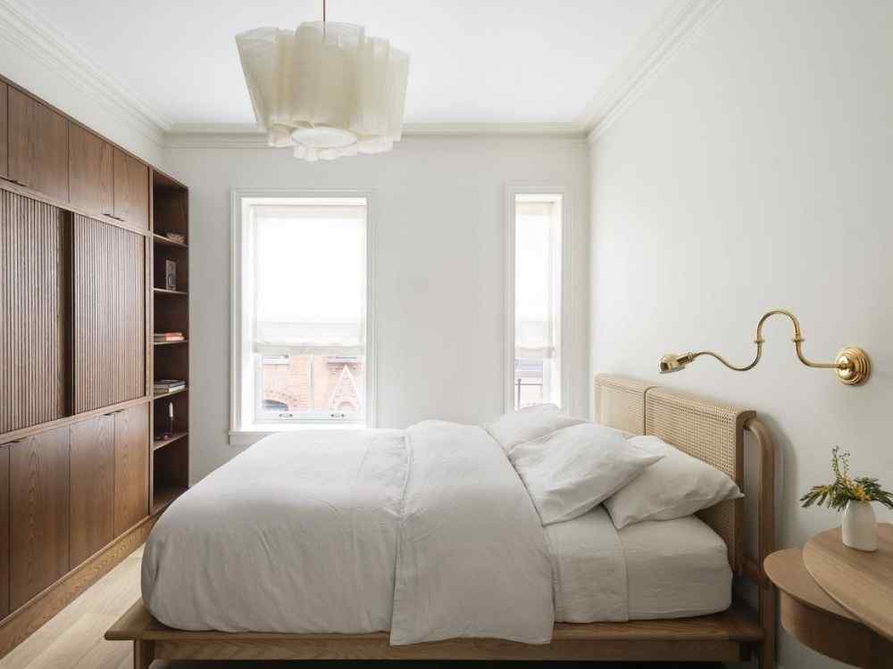 Phòng ngủ tối giản với nội thất gỗ, giường trắng đơn giản, tường trắng và đèn đọc sách gắn tường