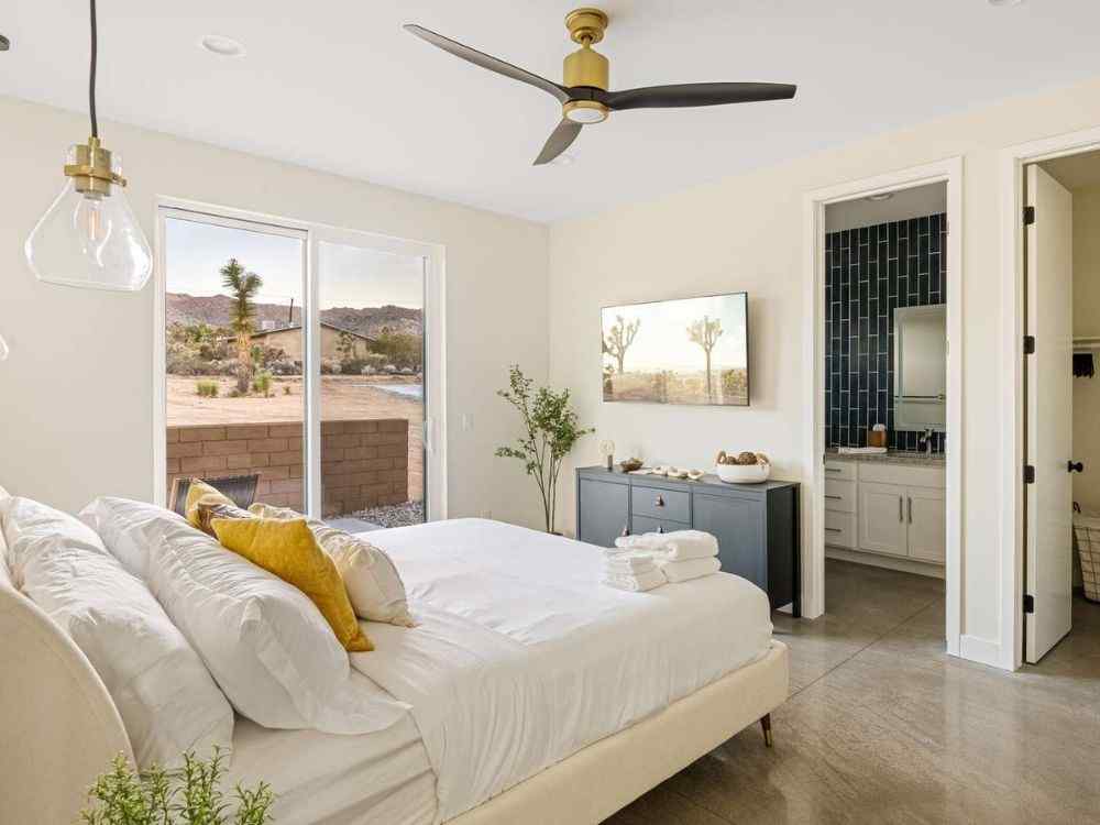 Phòng ngủ tông be sáng có cửa kính lớn nhìn ra sân, toilet riêng tông xanh than