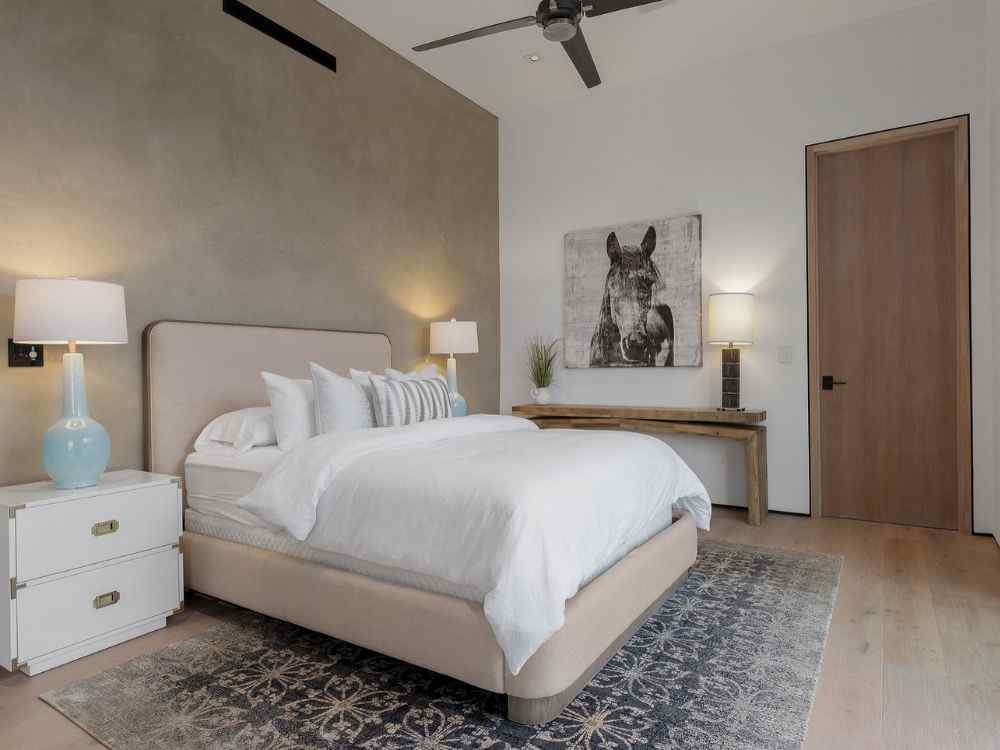 Phòng ngủ với giường bọc vải sáng, thảm hoa văn xám, tranh ngựa treo tường và đèn ngủ hai bên