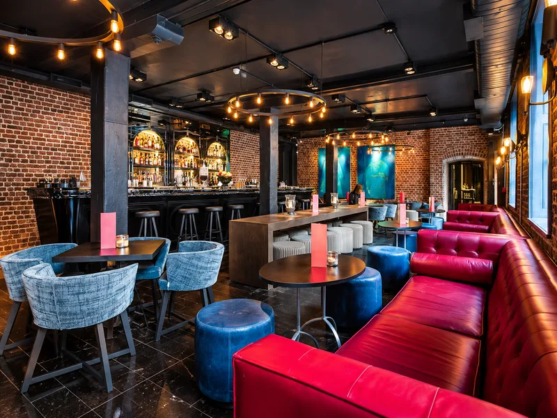 Quầy bar phong cách Funky phối ghế xanh và đỏ trước tường gạch trong không gian có nhiều đèn trang trí.