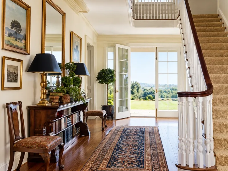 Sảnh nhà phong cách Farmhouse đặt bàn console gỗ dọc cầu thang trắng trên nền thảm dài.