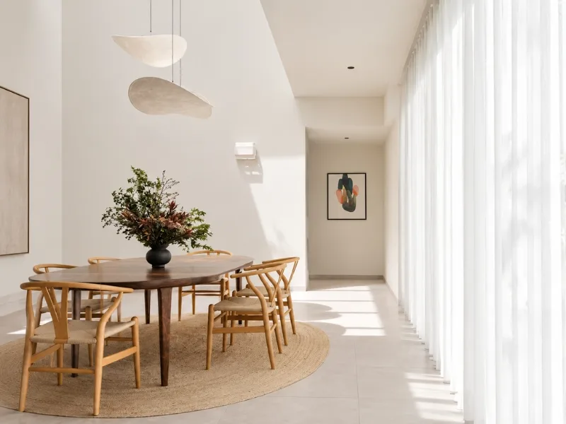Thiết kế phòng ăn phong cách Luxury đặt bàn gỗ dài cùng ghế thanh mảnh cạnh mảng tường trắng bo cong.